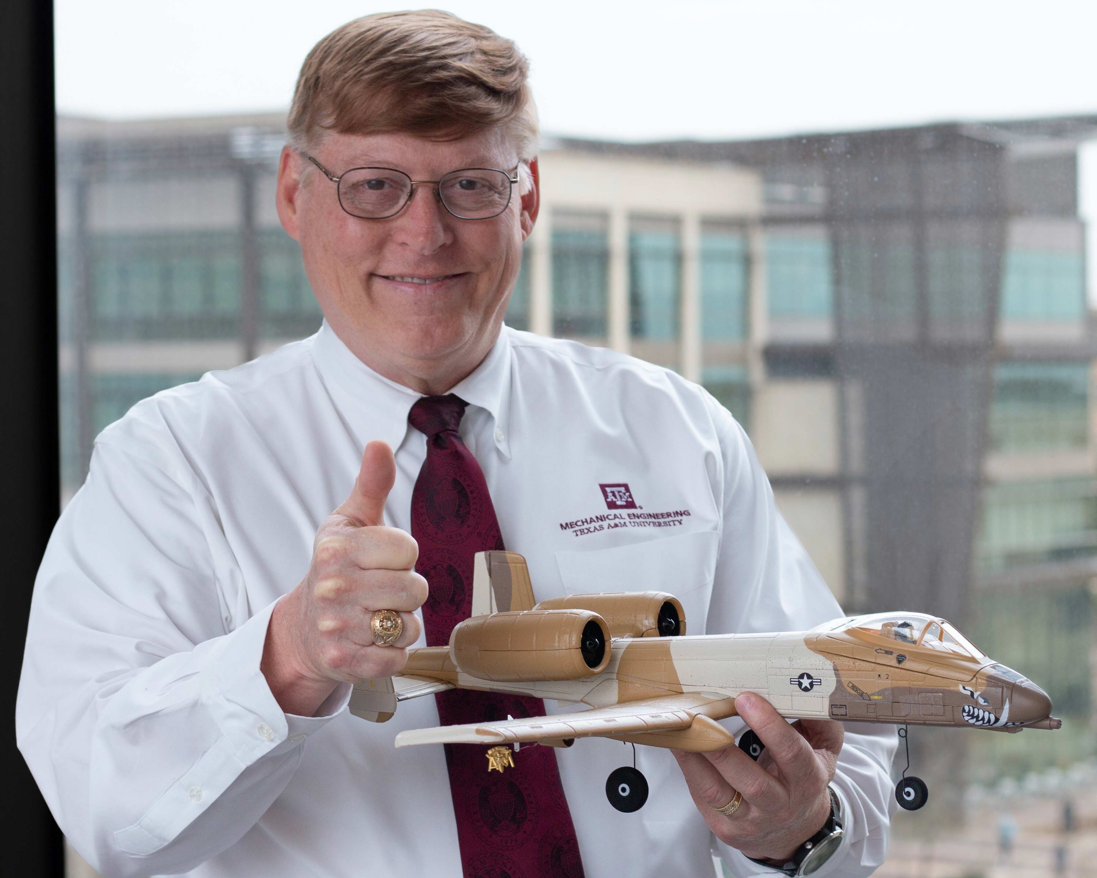 A man holds a model aircraft with his thumb up.