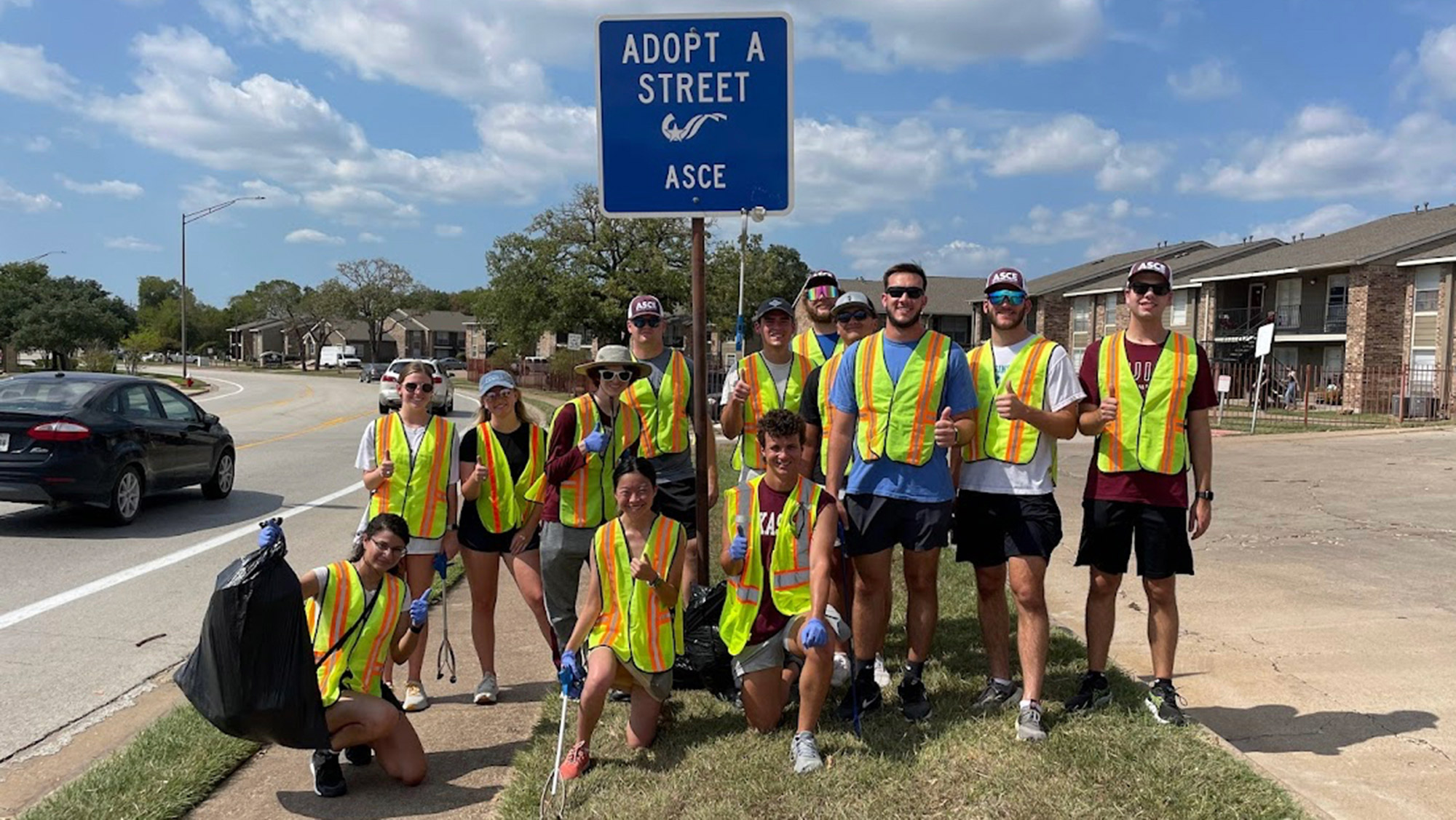 A group of people in construction vests in front of a road sign that reads Adopt a street ASCE.