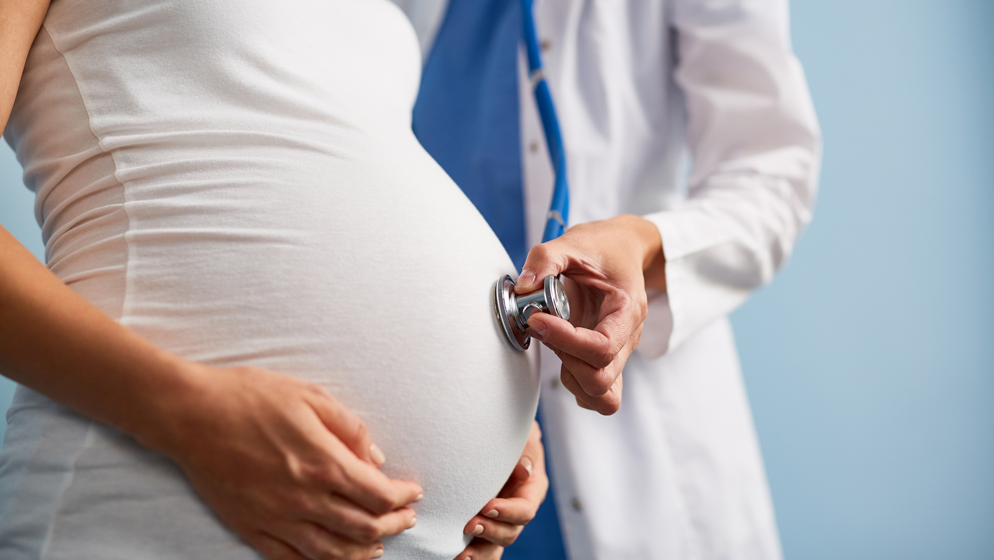 A picture of a doctor using a stethoscope on a pregnant woman's belly.