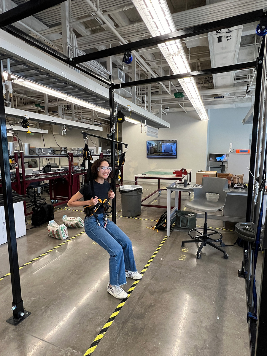 Woman sitting on a swing hanging from an overhead frame in an industrial workspace.