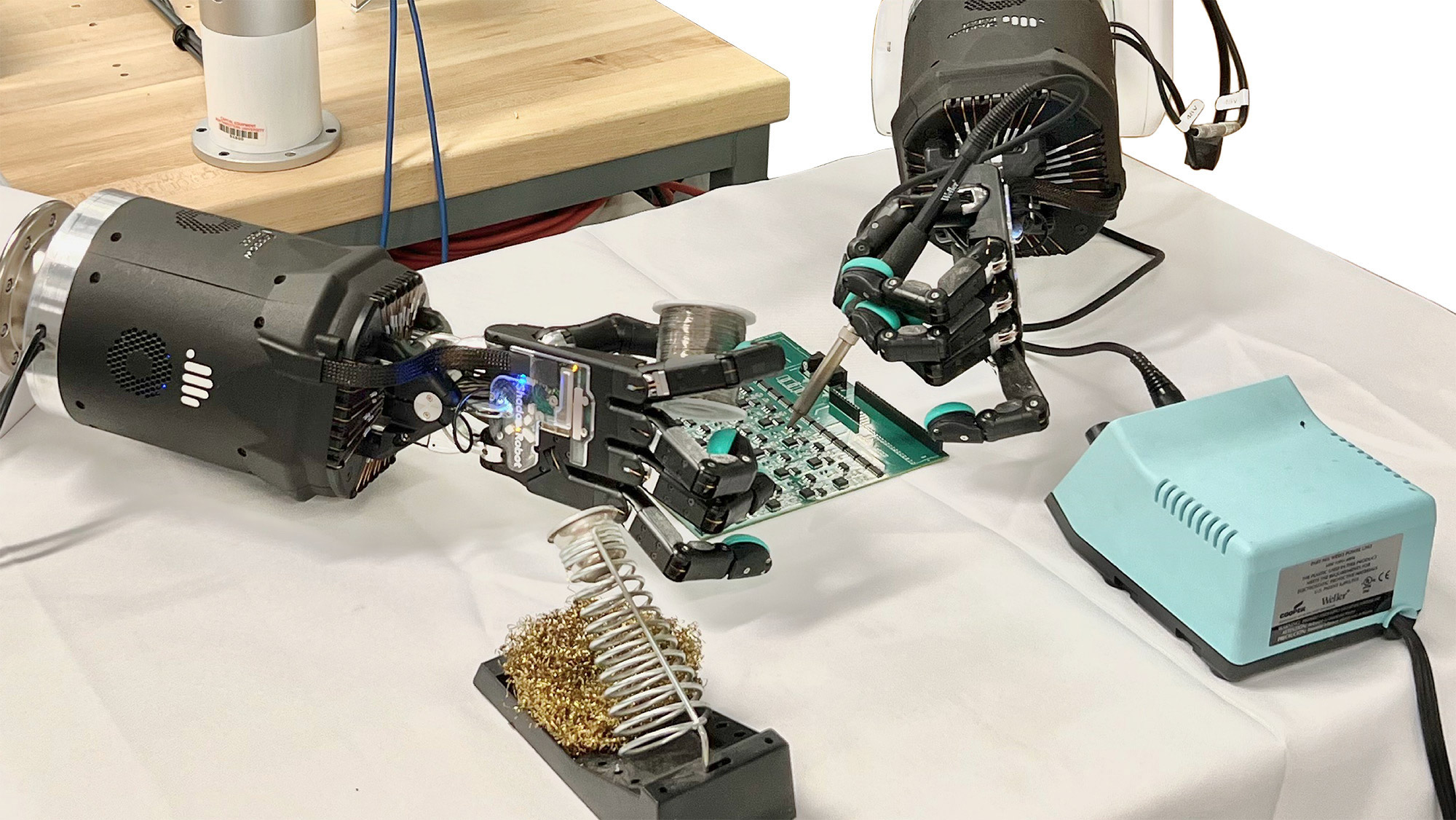 A close-up of two robotic hands soldering a motherboard on a table.