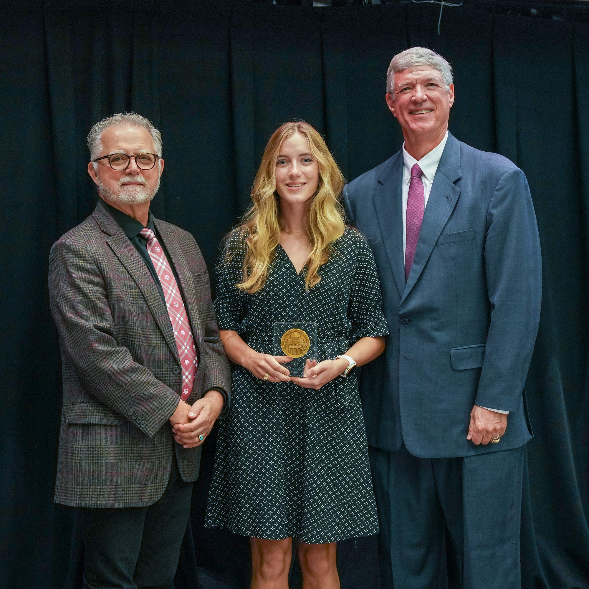 Two men standing next to woman with an award.