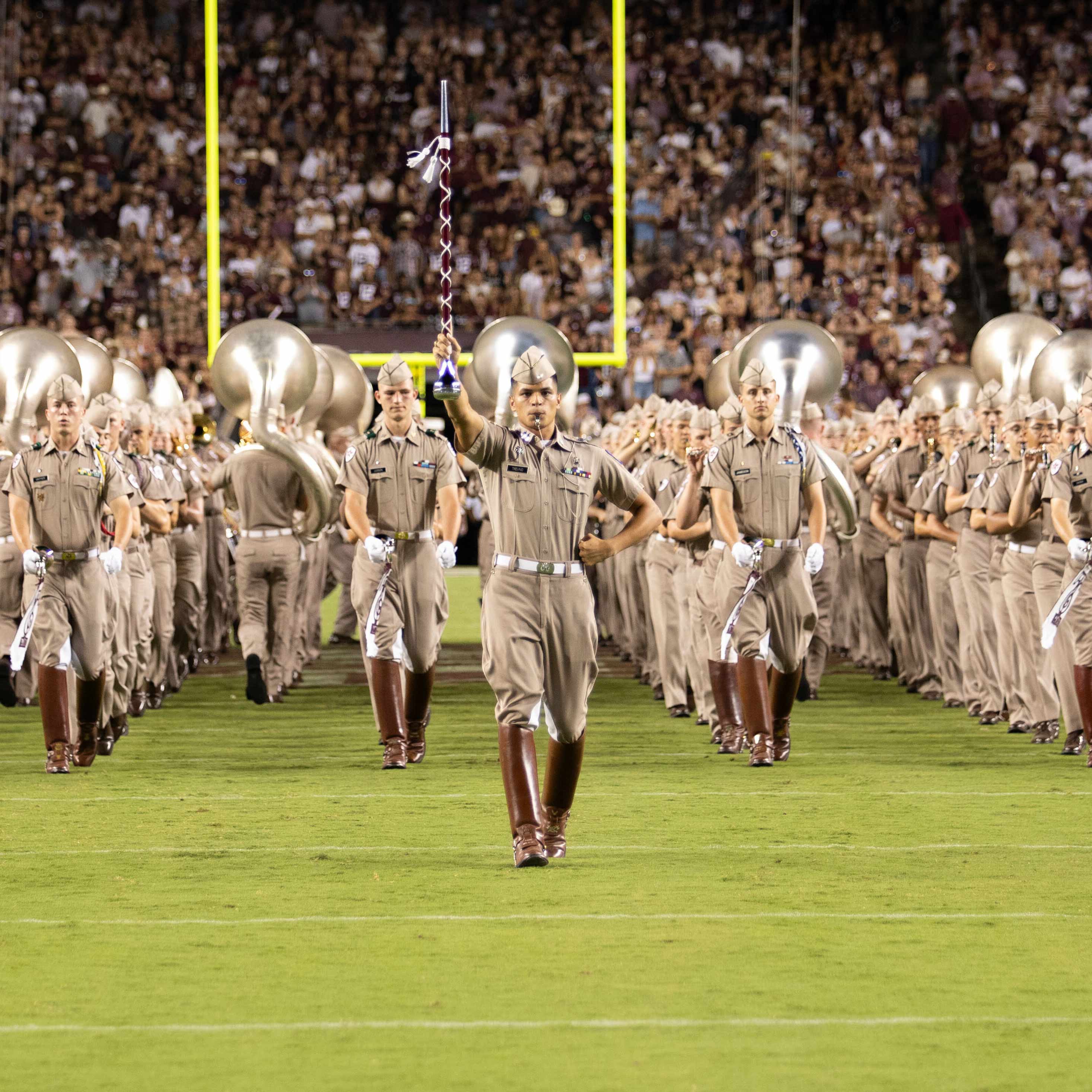 Band wearing military uniforms standing in formation on a football field.