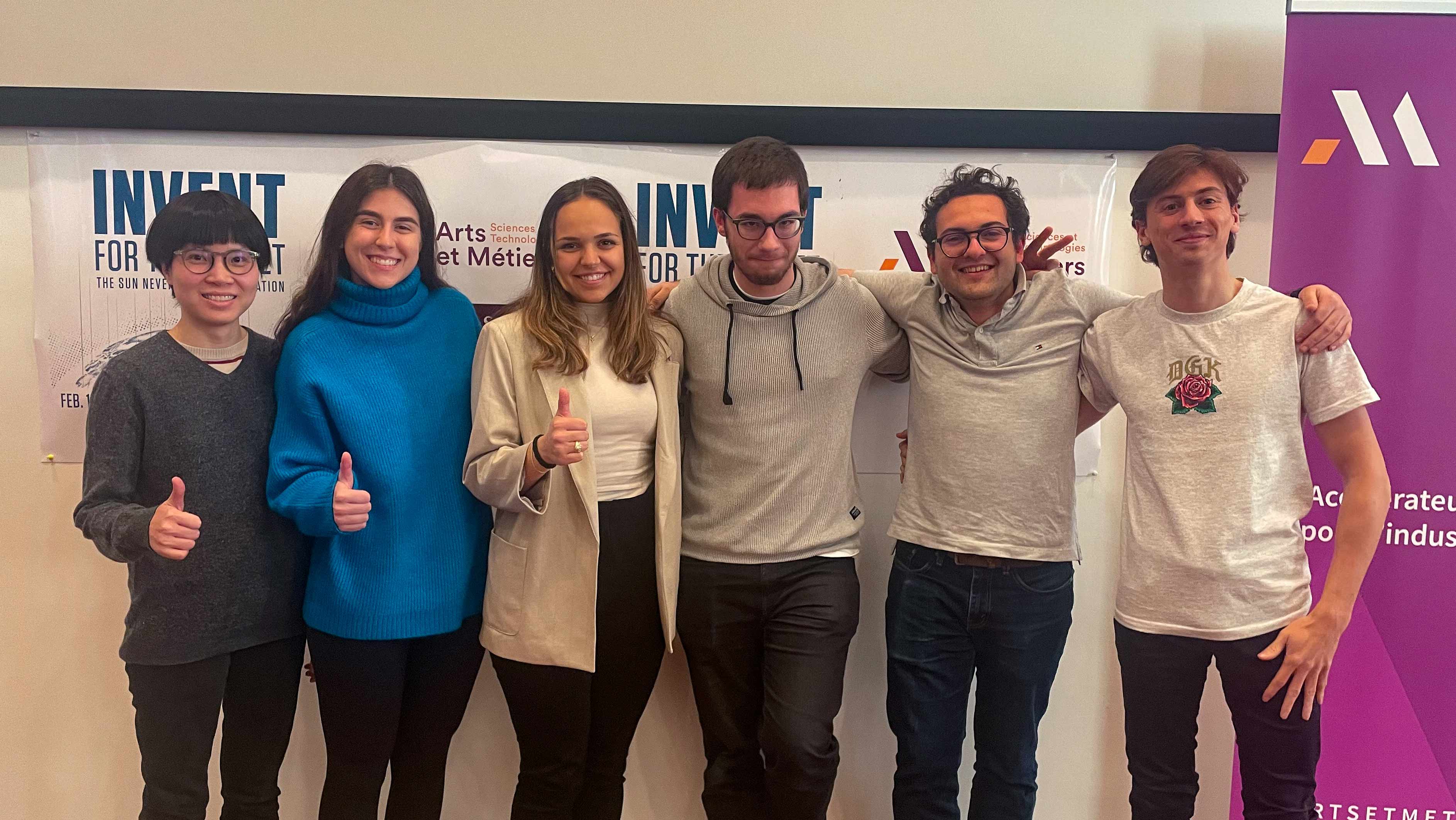 Five individuals standing together in front of a banner with INVENT for the Planet text, giving thumbs up and smiling.