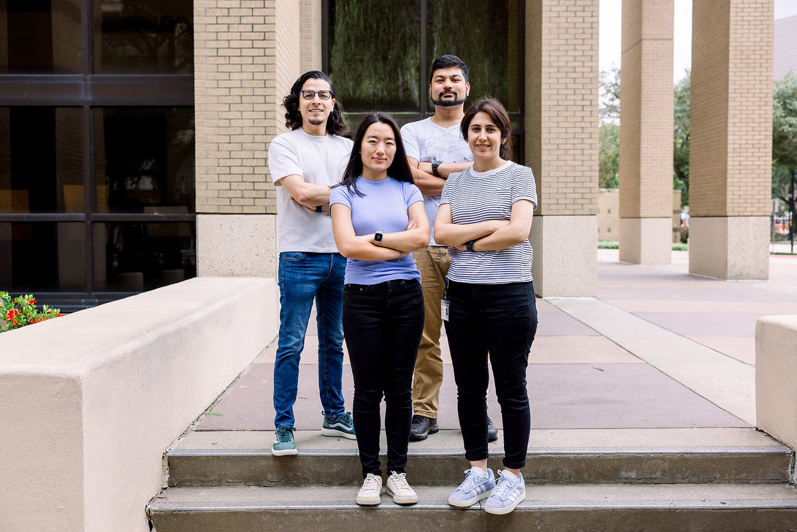 A group of students standing on the steps of a building with their arms crossed, smiling. 