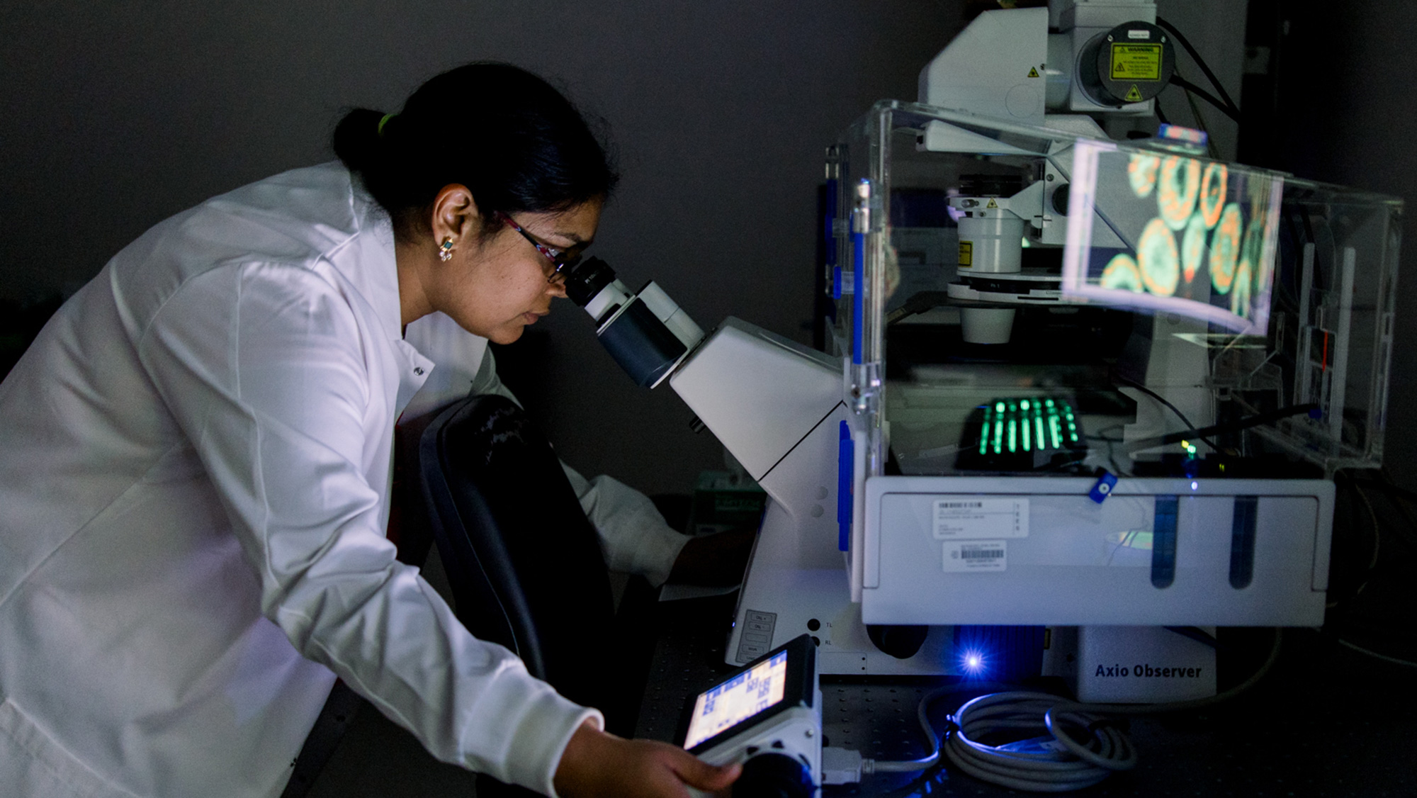 A researcher peers into a device with a white lab coat while spinning a dial.