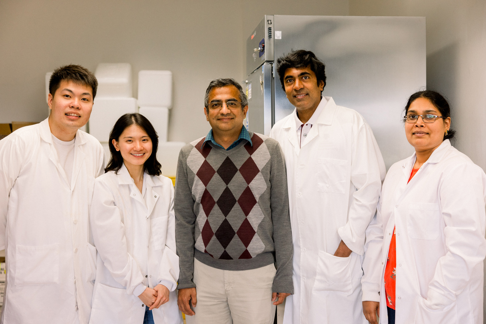  A group of researchers standing in a lab with white coats, smiling. 