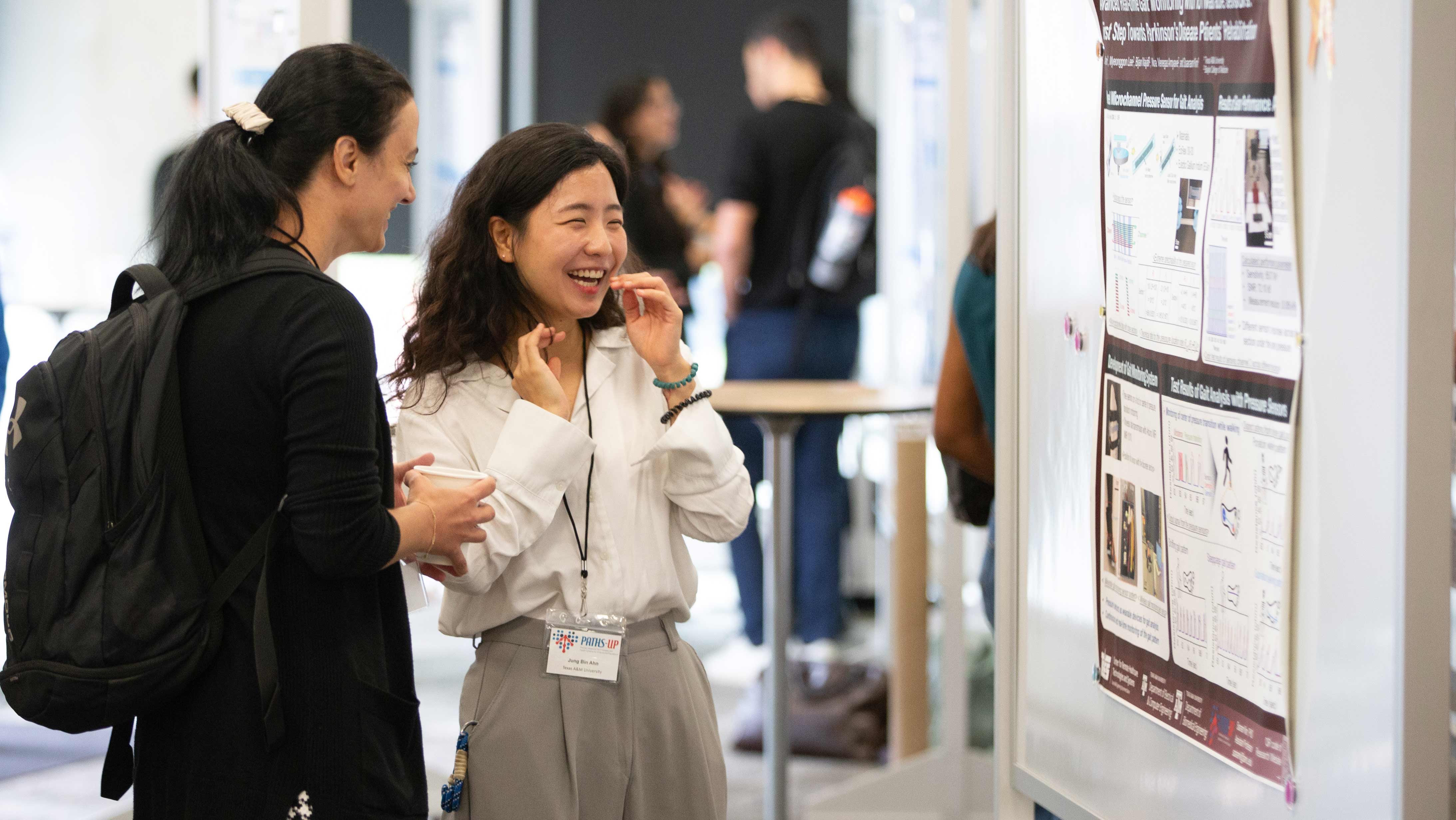 Two people laughing together in front of a research poster.