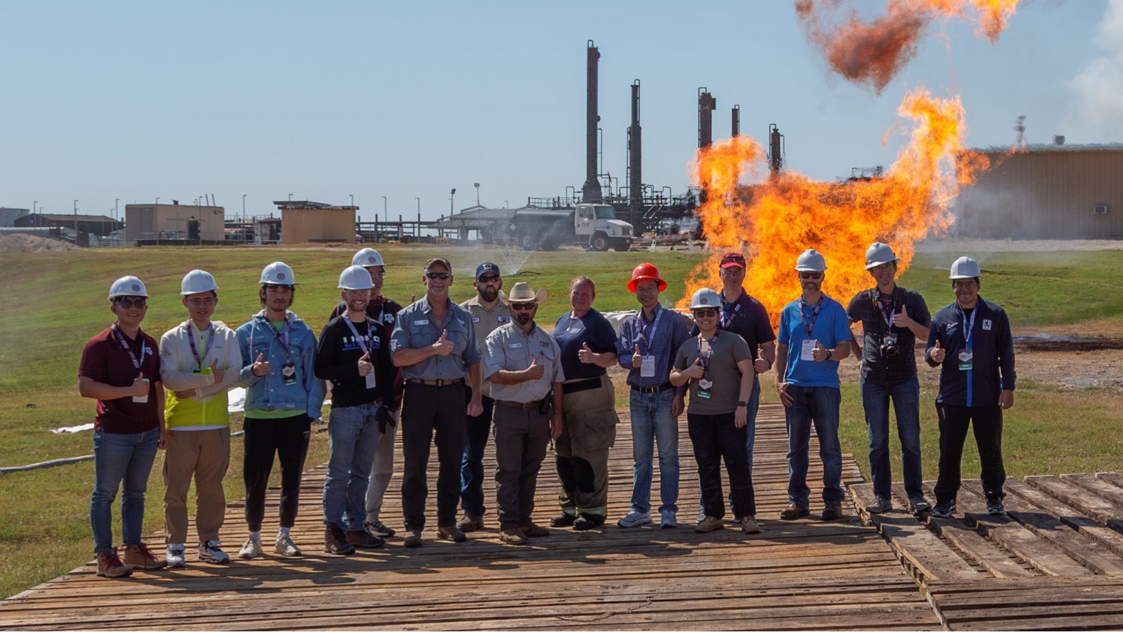 A group of people giving thumbs up with a controlled flame flare-up in the background.