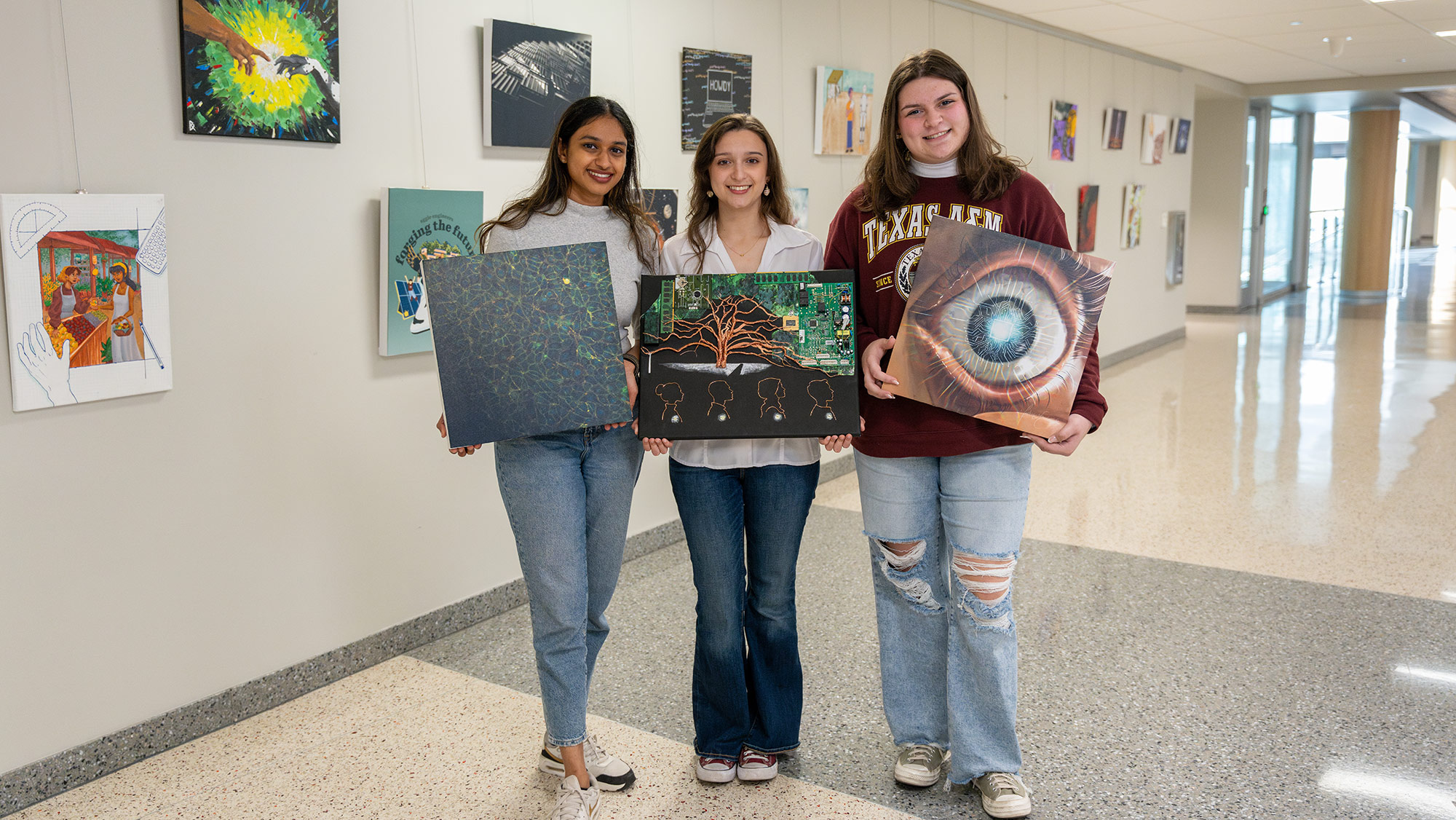 Three students holding their artwork and smiling.