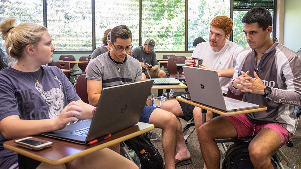 A group of undergraduate students gather their desks together to work collaboratively on a project presented in class.