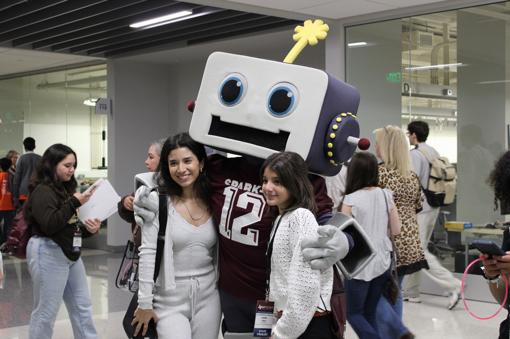 Spark-e robot stands with arms around two students