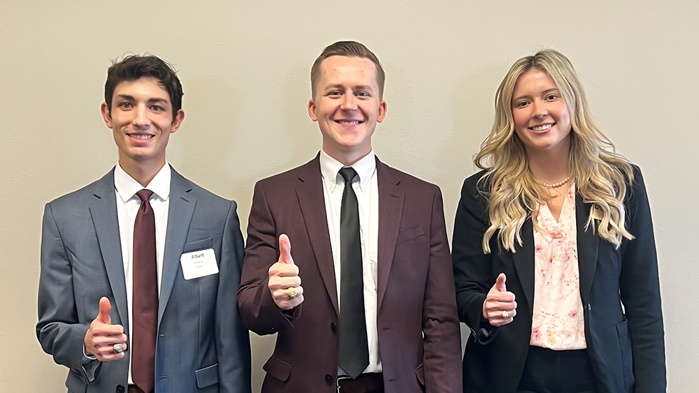 Three senior-level college students in business attire standing in a row and smiling.